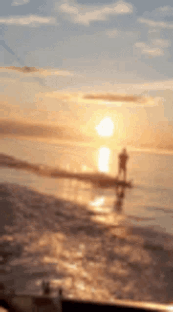 a blurry picture of a sunset with a person on a surfboard in the foreground