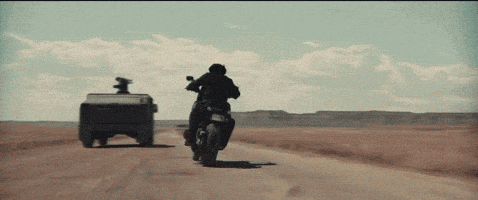 a man on a motorcycle is driving down a dirt road