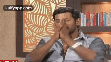 a man is covering his face with his hands while sitting on a couch .
