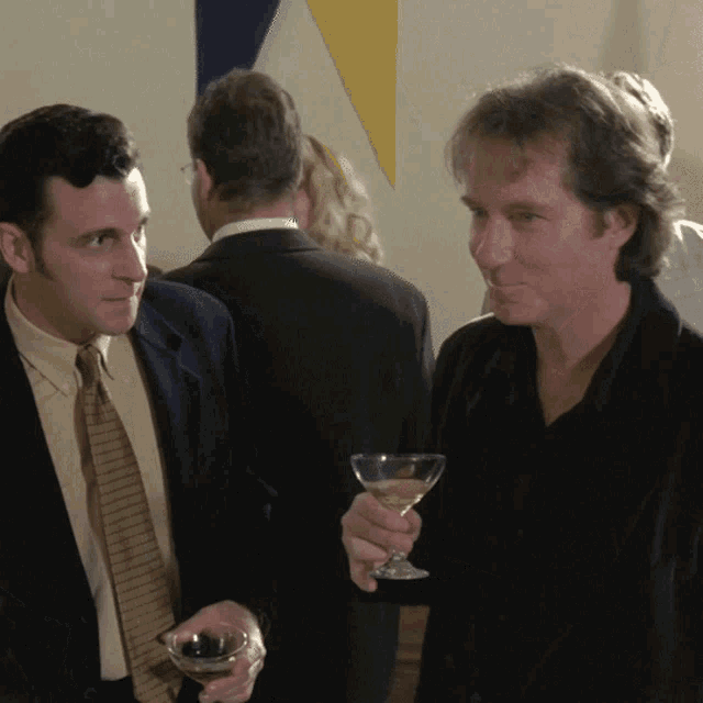 a man in a suit holds a glass of wine while talking to another man