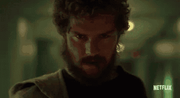 a man with a beard and curly hair is standing in a dark hallway .