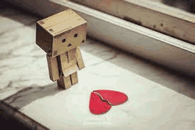 a cardboard box robot is standing next to a broken heart on a table .