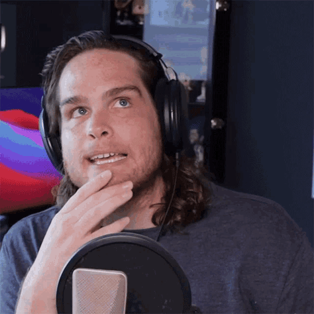 a man wearing headphones stands in front of a microphone making a funny face