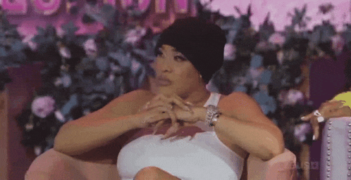 a woman wearing a black hat is sitting in a chair with her hands folded .