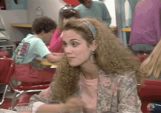 a woman with curly hair and a headband is sitting at a table in a diner .