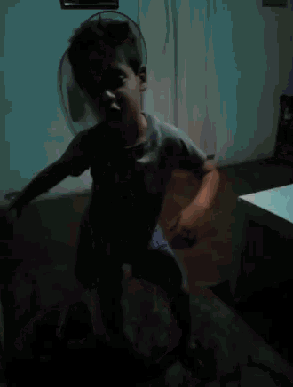 a young boy in a gray shirt and blue shorts is dancing in a dark room .