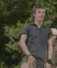 a man in a blue shirt is standing in front of trees .