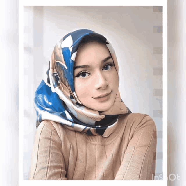 a woman wearing a blue scarf and a tan sweater is looking at the camera
