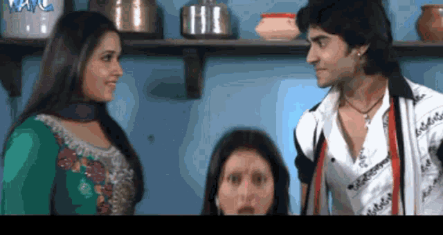 a man and a woman are standing next to each other in front of a shelf with a few pots on it
