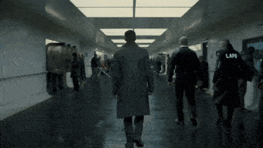 a man in a trench coat is walking down a hallway with two lapo officers behind him