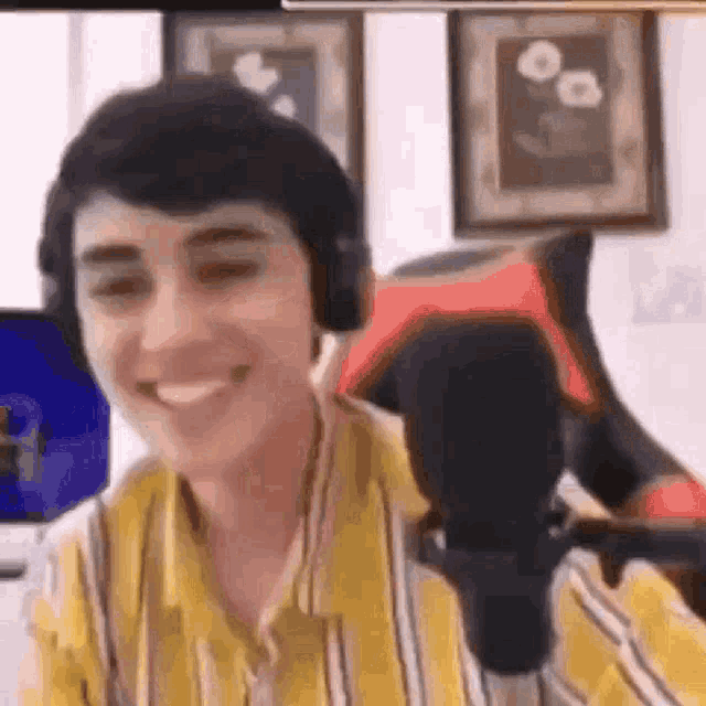 a young man wearing headphones is smiling while sitting in front of a microphone in a room .