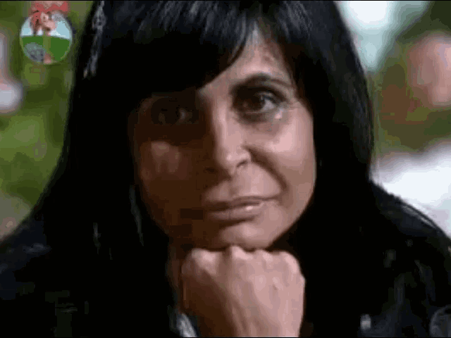 a woman with black hair is holding her hand to her chin and looking at the camera .