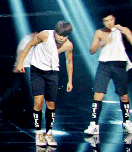 a man wearing a white tank top and black shorts has a pair of socks that say bts on them