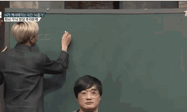 a man in a suit writes on a blackboard with foreign writing