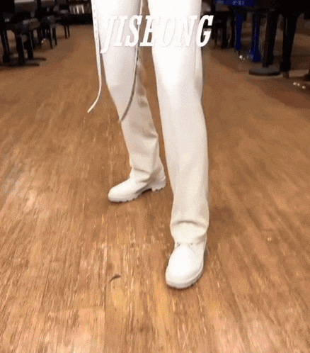 a person wearing white pants and white shoes with the word jisheng written on the floor