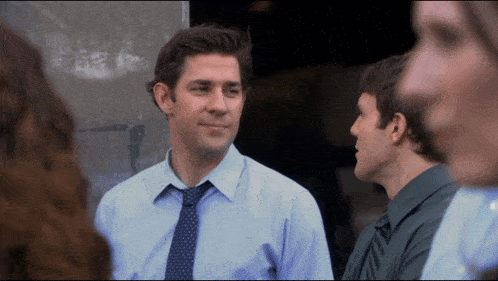 a man in a blue shirt and tie talks to another man in a green shirt