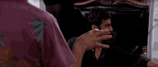 a man in a purple shirt is talking to another man in a black chair
