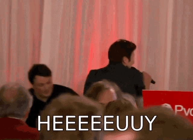 a man is giving a speech in front of a crowd and says heeeeeuuy