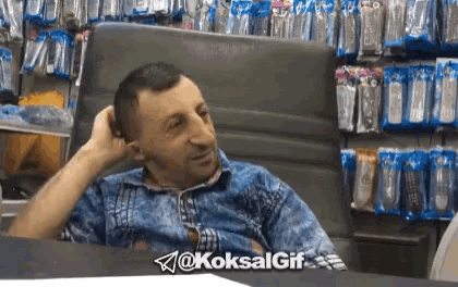 a man in a blue shirt is sitting in a chair in front of a shelf of remote controls