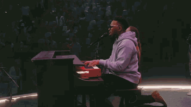 a man singing into a microphone wearing glasses and a grey hoodie
