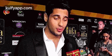 a man in a suit is talking into a microphone in front of a wall that says iifa