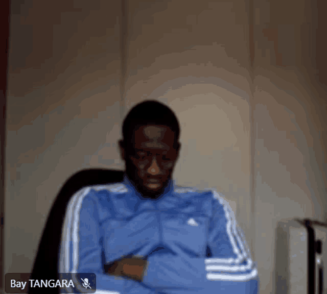 a man in a blue adidas jacket is sitting in a chair with his arms crossed