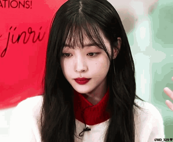 a girl with long black hair and red lipstick stands in front of a sign that says ' jinri '