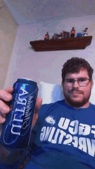 a man in a blue shirt holds up a can of artois