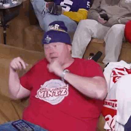 a man wearing a red shirt that says minot is sitting on a couch .