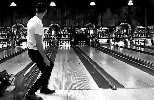 a man is playing bowling in a bowling alley in a black and white photo .