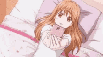 a girl is laying on a bed holding a phone in her hands .