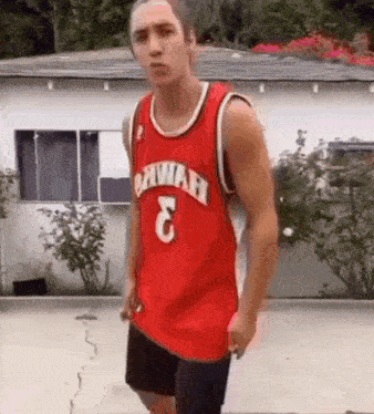 a young man wearing a red basketball jersey is standing in front of a house .