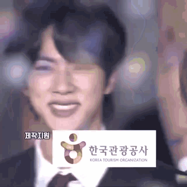 a man in a suit and tie is smiling in front of a korea tourism organization logo