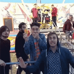 a group of men are standing in front of a carnival ride and one man is covering his mouth with his hand
