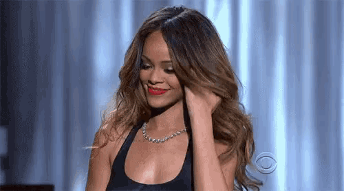 the woman is wearing a black tank top and a necklace and is smiling .