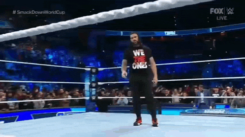 a wrestler wearing a black shirt that says we the ones is walking out of a wrestling ring .