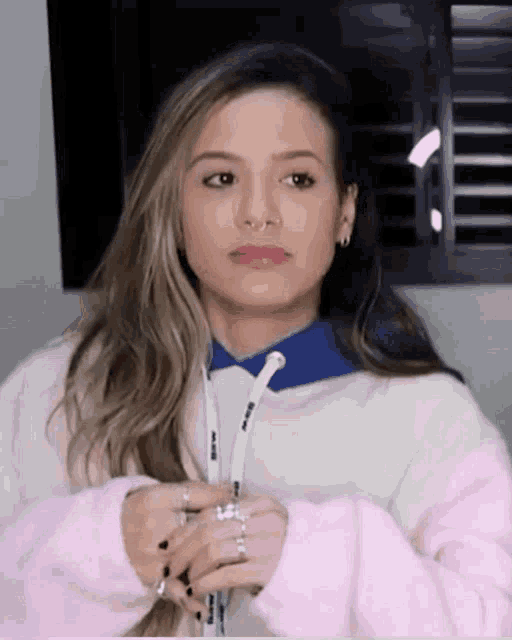 a woman wearing a pink and white sweatshirt with a blue collar looks at the camera