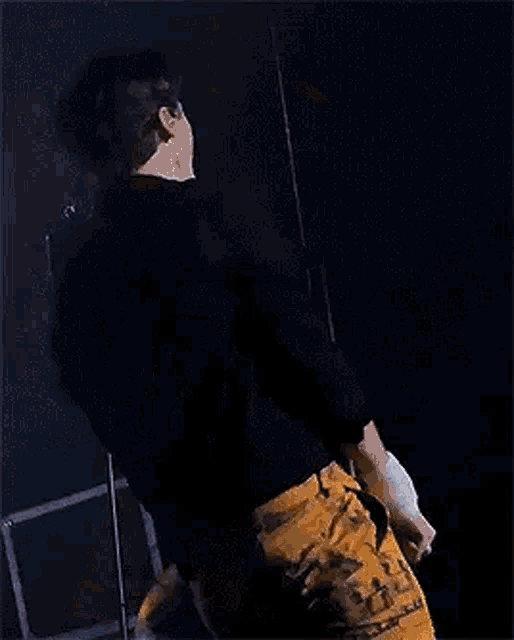 a man in a black jacket and yellow pants is standing on a stage in the dark .
