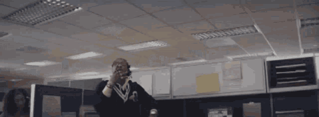 a man wearing sunglasses and a yellow hoodie is sitting in a cubicle in an office