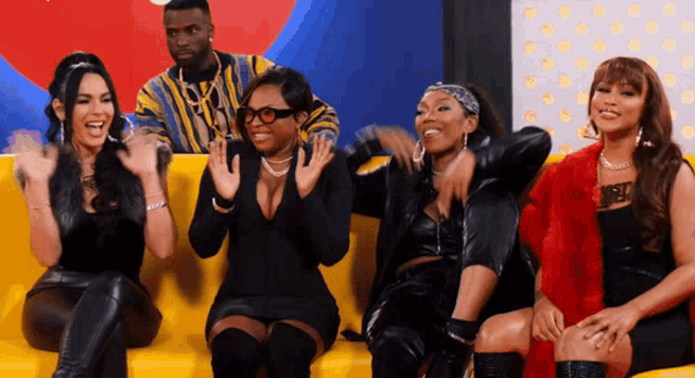 a group of women are sitting on a yellow couch with a man in a striped shirt