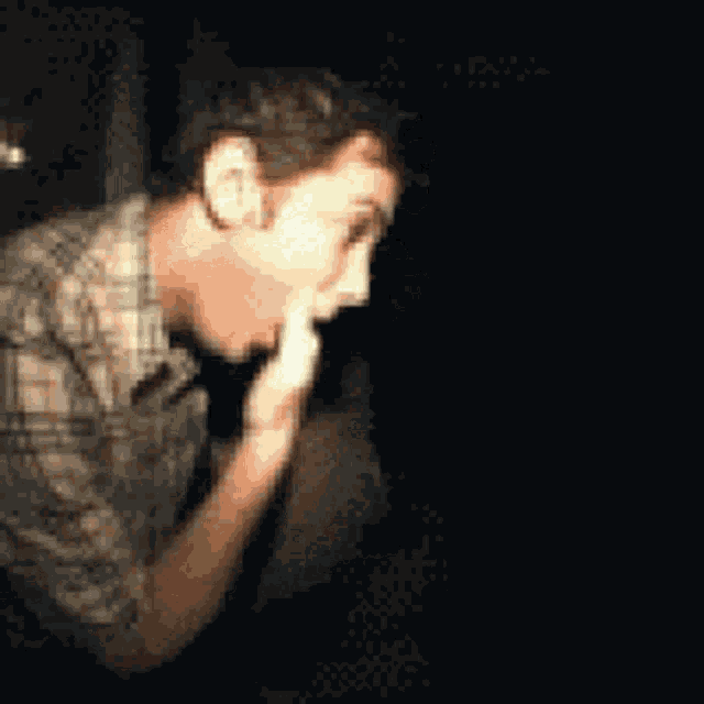 a man in a plaid shirt is covering his face with his hand