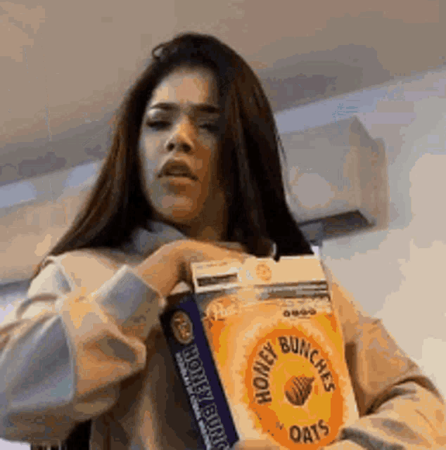 a woman is holding a box of honey bunches of oats in her hand .