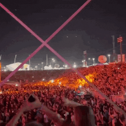 a crowd of people at a concert with a purple light beam coming out of the stands