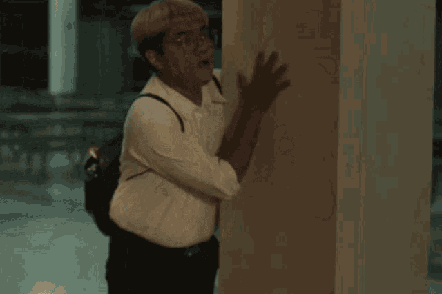 a woman wearing glasses and a white shirt stands in a dark hallway