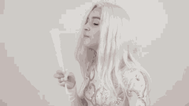 a woman with blonde hair is holding a fan in her hand and looking at it .