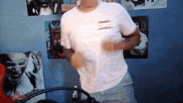 a man in a white t-shirt is dancing in front of a wall of pictures