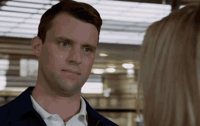 a man in a white shirt and blue jacket looks at a woman