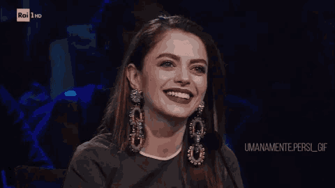 a woman wearing a pair of earrings is smiling in front of rai 1 hd