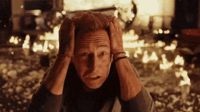 a man holds his head in front of a burning house