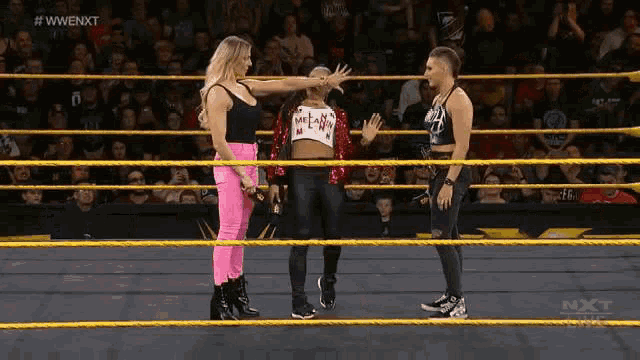 three women are standing in a wrestling ring .